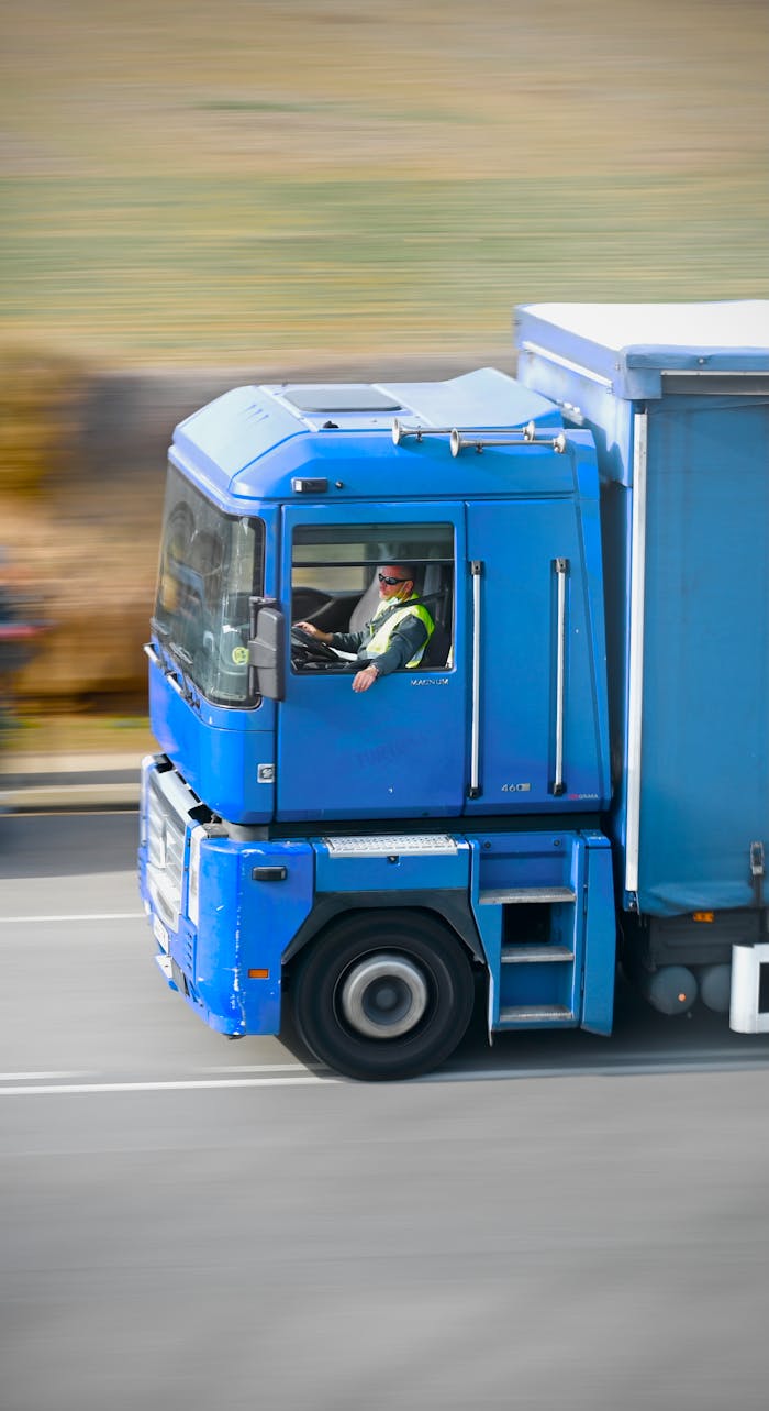 Dynamic panning shot capturing a blue truck in motion on a highway in daylight.