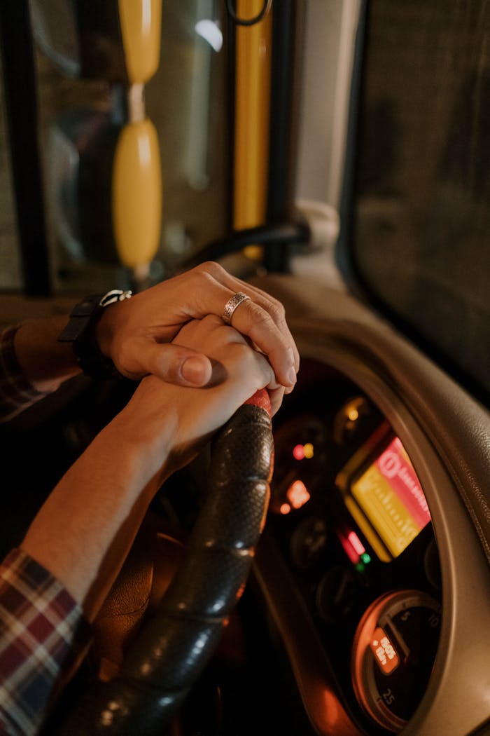 Hands with a ring on a steering wheel, suggesting companionship or teamwork.